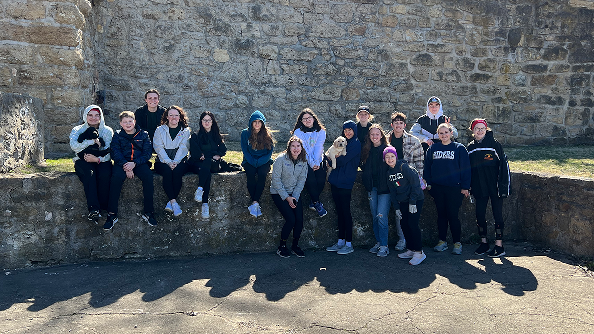 group of teens standing in front of large brick structure