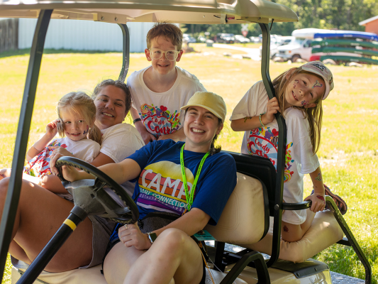 campers laughing with volunteers on golf cart